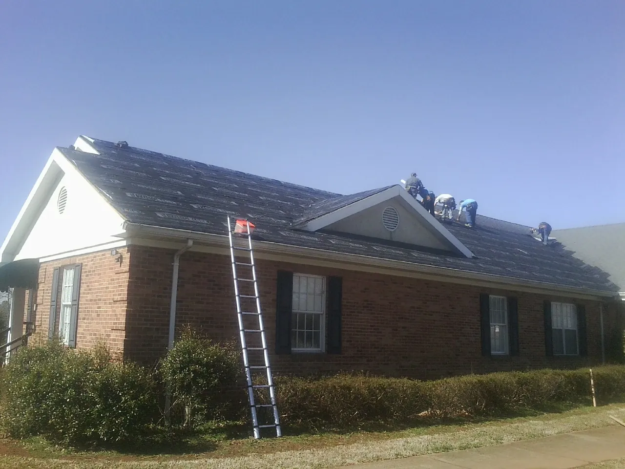 Crew tearing shingles off a brick ranch roof with a ladder set — Emergency Roof Repair work by our crew in Canajoharie