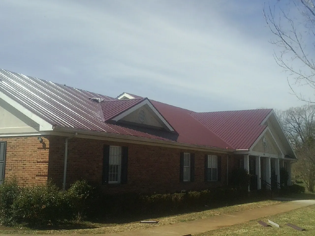 Red metal roof with gabled entries on a long brick building, from a Hail Damage Roof Repair job in Canajoharie
