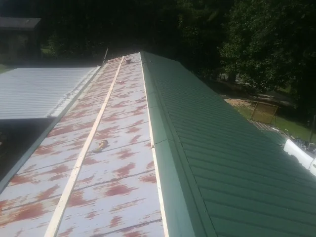 Old rusted panels beside newly installed green metal roofing — Wind Damage Roof Repair by Roofing Brothers in Canajoharie