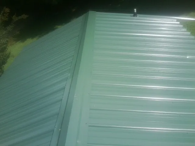 New green metal panels meeting at the ridge of a roof — Flat Roof Repair work by our crew in Canajoharie