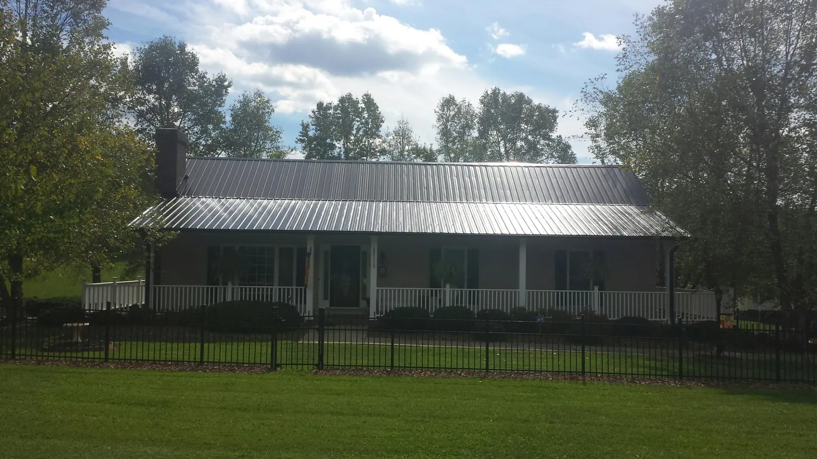 Gray metal roof on a brick ranch with a full width front porch — Gutter Guard Installation work by our crew in Canajoharie