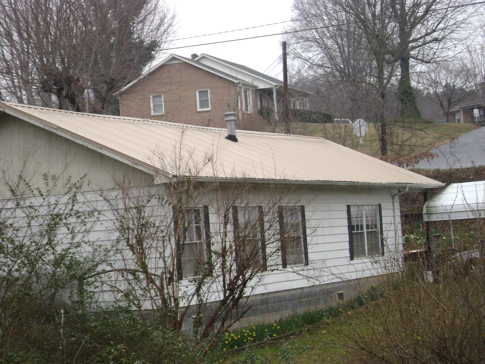 Tan metal roof on a white sided house set into a hillside — Commercial Roofing by Roofing Brothers in Canajoharie