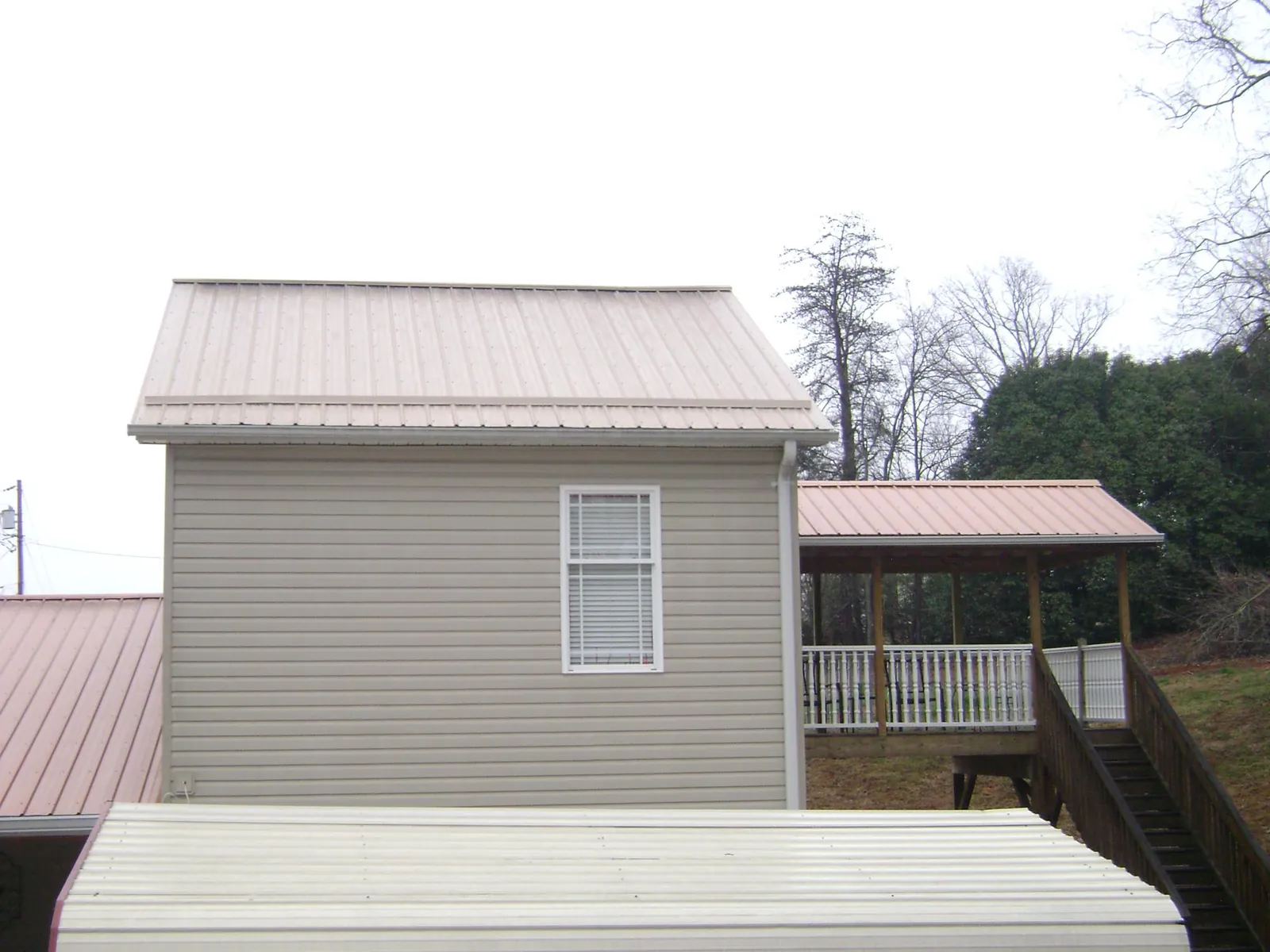 Tan metal roofs on a two story addition and attached porch, from a Roof Replacement job in Canajoharie